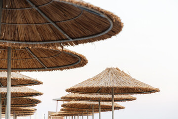 Rows of thatched straw beach umbrellas against a bright sky. Ideal for tropical vacation and summer travel themes © serebryannikov