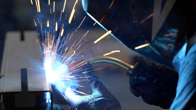 Striking close-up of bright sparks flying from heavy industrial equipment during a metalworking process. The image captures the intense heat and dynamic energy of modern manufacturing