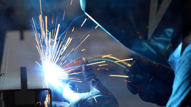 Striking close-up of bright sparks flying from heavy industrial equipment during a metalworking process. The image captures the intense heat and dynamic energy of modern manufacturing