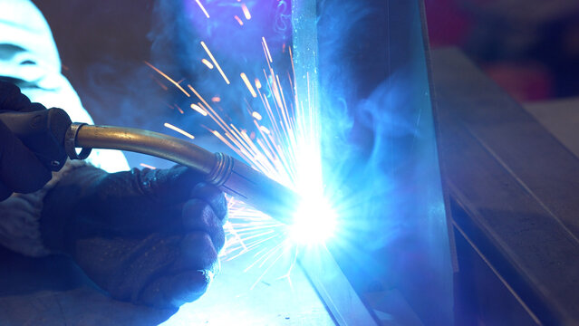 Striking close-up of bright sparks flying from heavy industrial equipment during a metalworking process. The image captures the intense heat and dynamic energy of modern manufacturing