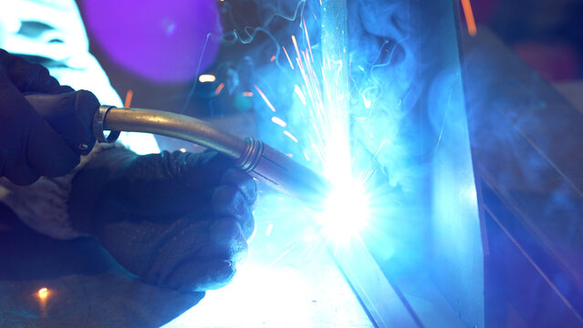 Striking close-up of bright sparks flying from heavy industrial equipment during a metalworking process. The image captures the intense heat and dynamic energy of modern manufacturing