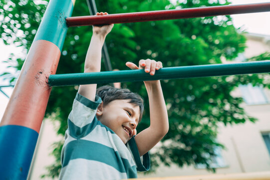 A happy boy is climbing on a playground bar during the summer