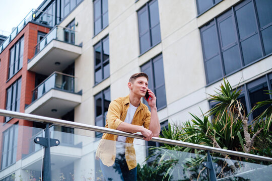 Smiling man talking through smart phone leaning on railing