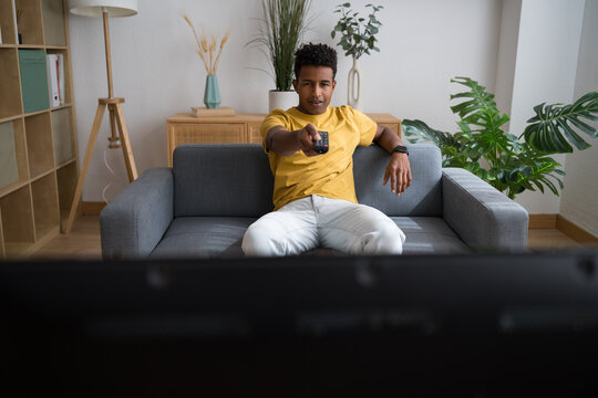 Man relaxing on sofa and watching TV indoors with remote control
