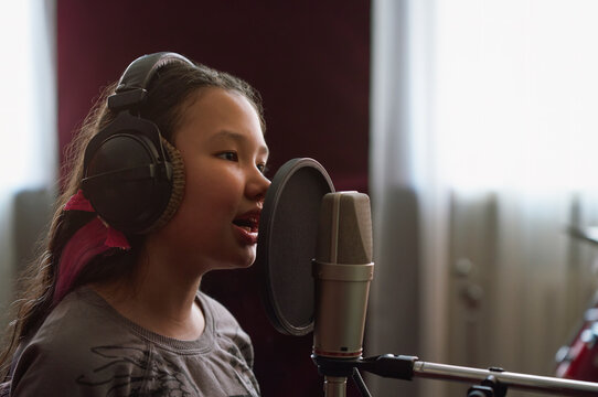 Girl recording song on microphone in studio