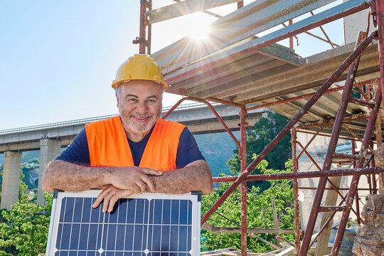 Smiling technician holds a solar panel at a construction site