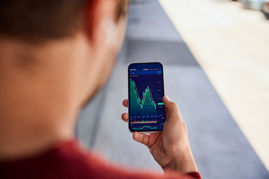 Investor analyzing stock market chart on smartphone app outdoors