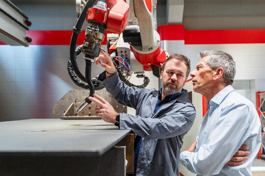 An engineer and a manager inspect an industrial robot in a factory