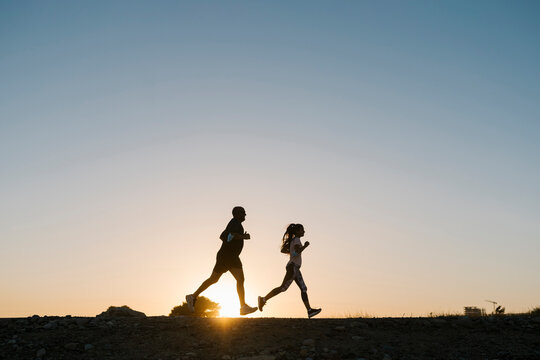 Silhouette of athlete and woman running against clear sky during sunset
