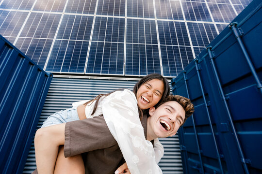 Happy man gives piggyback ride to woman near solar panel