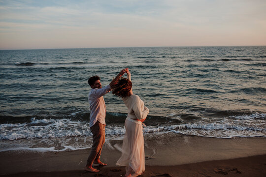 Expecting couple dancing on the beach at sunset