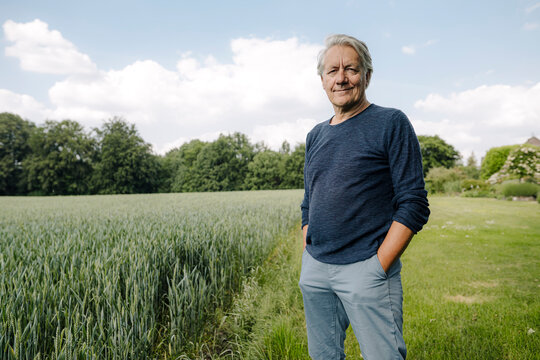 Smiling man with hands in pockets standing in field