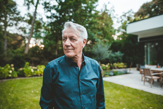 Senior man with white hair standing at backyard