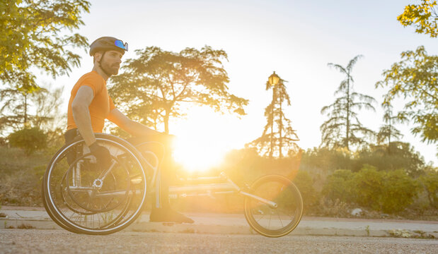 Athlete sitting in wheelchair on road at sunset