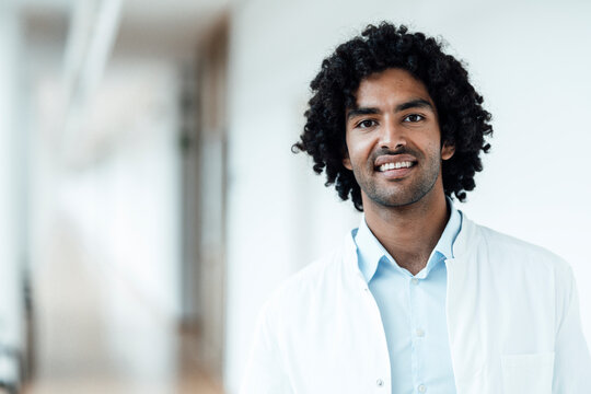Smiling young male doctor with black curly hair at hospital corridor