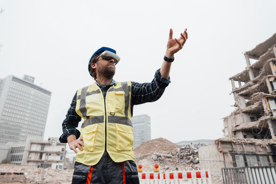 Worker wearing virtual reality glasses gesturing in front of construction site