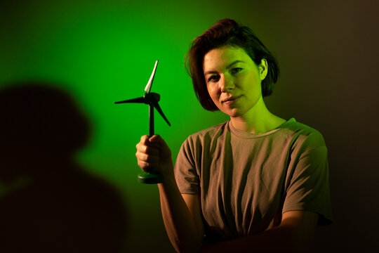 Smiling young businesswoman with wind turbine model standing against colored background