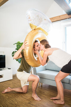 Affectionate couple kissing through large inflatble ring at home