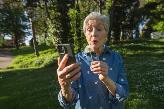 Senior blowing dandelion while taking selfie outdoors