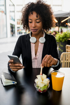 Portrait of businesswoman looking at cell phone at pavement cafe while eating fruit salad