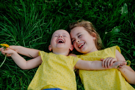 Two laughing sisters lying on a meadow wearing yellow tops
