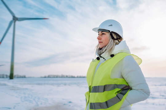 Engineer with hands in pockets standing near wind turbine in winter