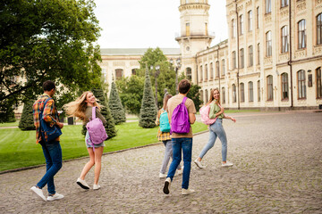 Obraz premium Happy university students walking across a historic campus courtyard with backpacks and laughing friends