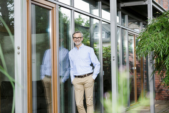 Smiling man leaning against facade of his house