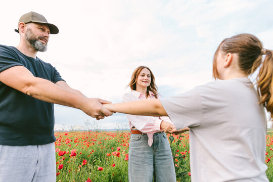 Man woman and girl hold hands playfully in a poppy field