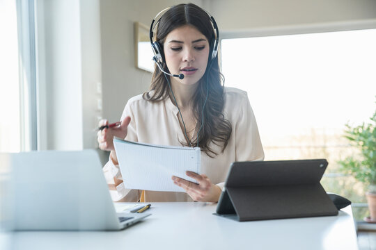 Young woman sitting at table at home wearing a headset