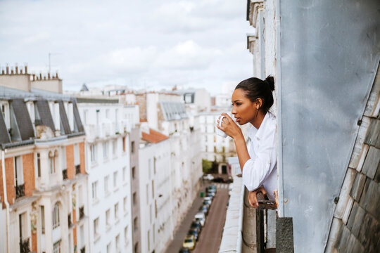 France, Paris, young woman with cup of coffee leaning out of window