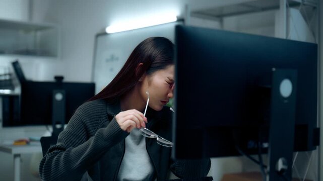 Female software developer adjusting her eyeglasses working late computer, expressing stress workload burnout concentration software engineering artificial intelligence modern IT workplace concepts