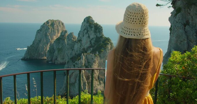 Tourist woman reading map while admiring Faraglioni cliffs from lookout in Capri Italy