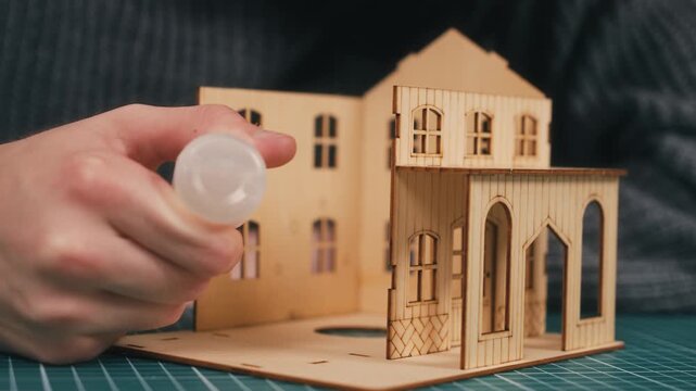 Completing miniature house assembly with glue application and final wall placement. DIY wooden home model nearing completion, hands crafting architectural structure, new housing concept, maker