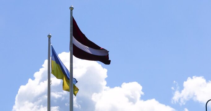 Ukrainian and Latvian flags against a blue sky in windy weather. Support Ukraine