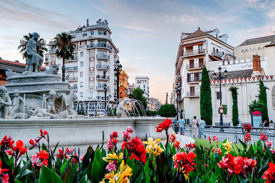 City fountain with flowers and people in Seville, H&iacute;spalis Fountain. People on streets city with beautiful architecture, an urban scene, Spain.