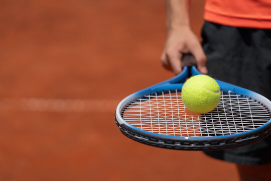 Close-up of tennis ball resting on racket held by teenage player on an outdoor clay court with copy space.