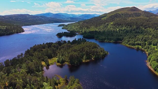 Aerial drone view over Loch Beinn Mheadhoin in Glen Affric, Scotland, with forested islands, blue water and Highland mountains under a bright sky. 4K UHD video.