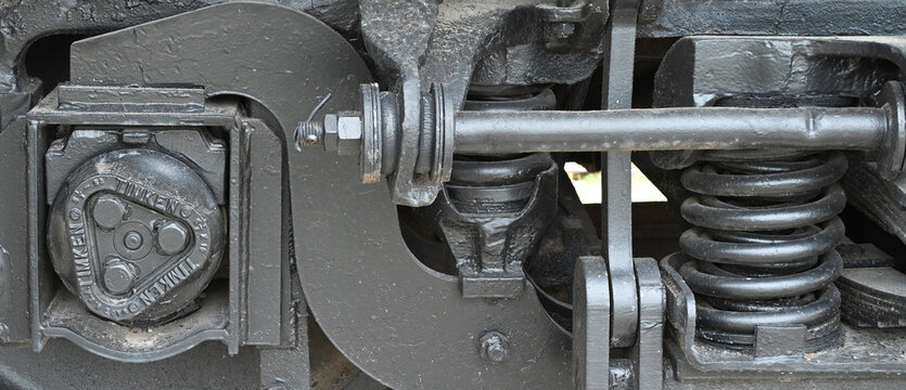 Horizontal close up of a black painted steel train wheel assembly with coil springs, metal housing, bolts, nuts, smooth and rough surfaces, and visible industrial components