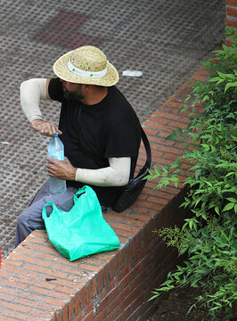 Beber agua golpe de calor hidratar botella l&iacute;quido refrescar muerte por calor verano insolaci&oacute;n lipotimia mojarse se&ntilde;or sombrero de paja hidrat&aacute;ndose sentado en ladrillo water bottle hydrate refresh 