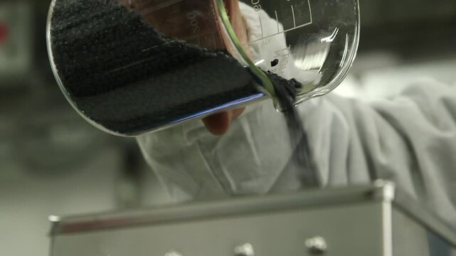 Technician pouring black plastic pellets into laboratory processing equipment before polymer extrusion and material testing in an industrial research environment.