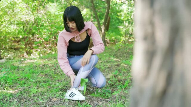 Injured female hiker ankle ache sitting on trail, clutching her leg in pain, stop training to massage joint ache on path while resting during a trek in a scenic mountain landscape, accident in workout