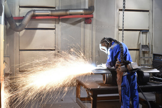 Workers in protective equipment in a foundry work on a casting with a grinding machine at the workplace