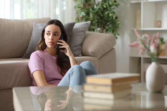 Serious woman making phone call looking at side sitting at home