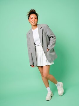 Young Asian Woman Wearing Gray Blazer and Pleated Skirt Posing Against Pastel Green Background