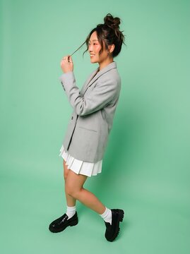 Stylish Young Asian Woman Posing in a Gray Blazer and White Pleated Skirt on Green Background