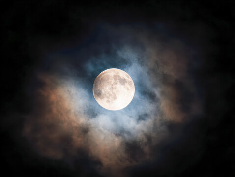 Full moon glowing brightly in the night sky surrounded by colorful clouds creating a mystical and captivating lunar atmosphere in nature