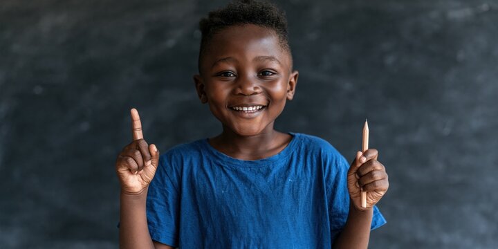Smiling child holding a pencil and pointing up with index finger against a chalkboard for school learning poster and educational banner
