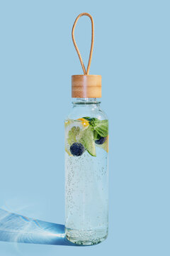Reusable glass bottle containing refreshing fruit-infused water with lemon, cucumber, and blueberries