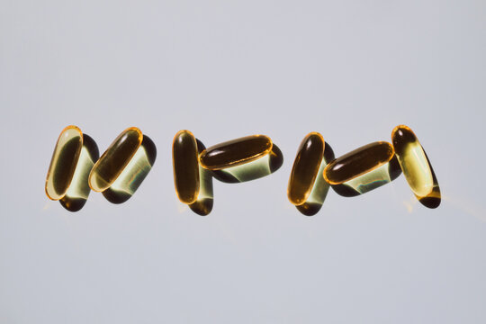 Yellow softgel capsules casting shadows on light background